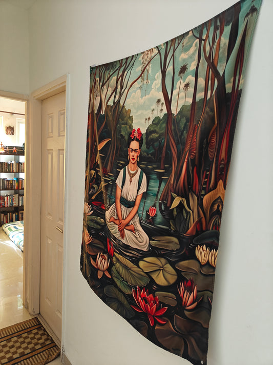 A bohemian style tapestry featuring a stylized depiction of Frida Kahlo with a floral backdrop, seated in a meditation pose, displayed on a wall.
