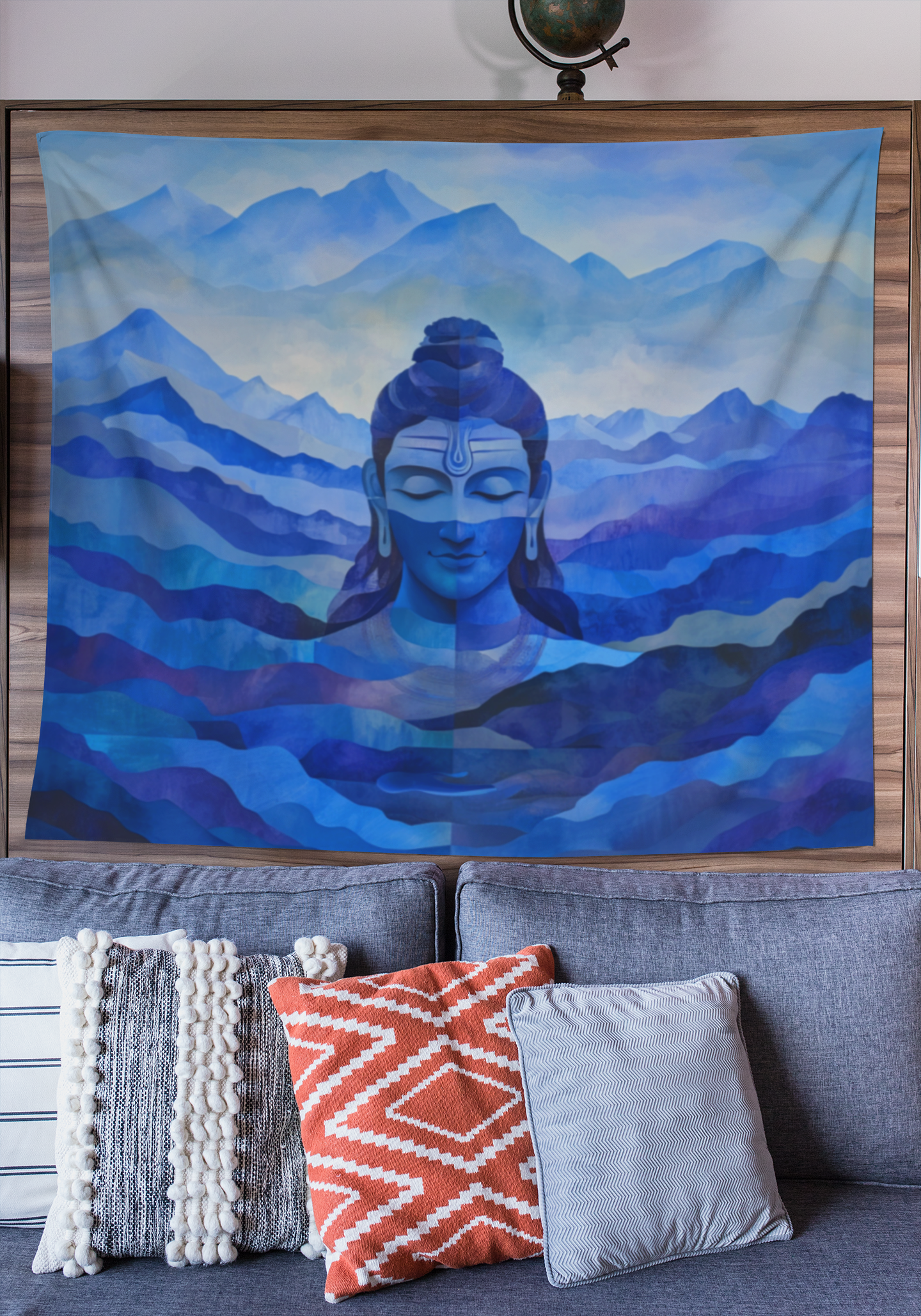 A wall art tapestry featuring a blue depiction of Lord Shiva with mountains in the background, displayed on a wall above a couch with various pillows arranged in front.