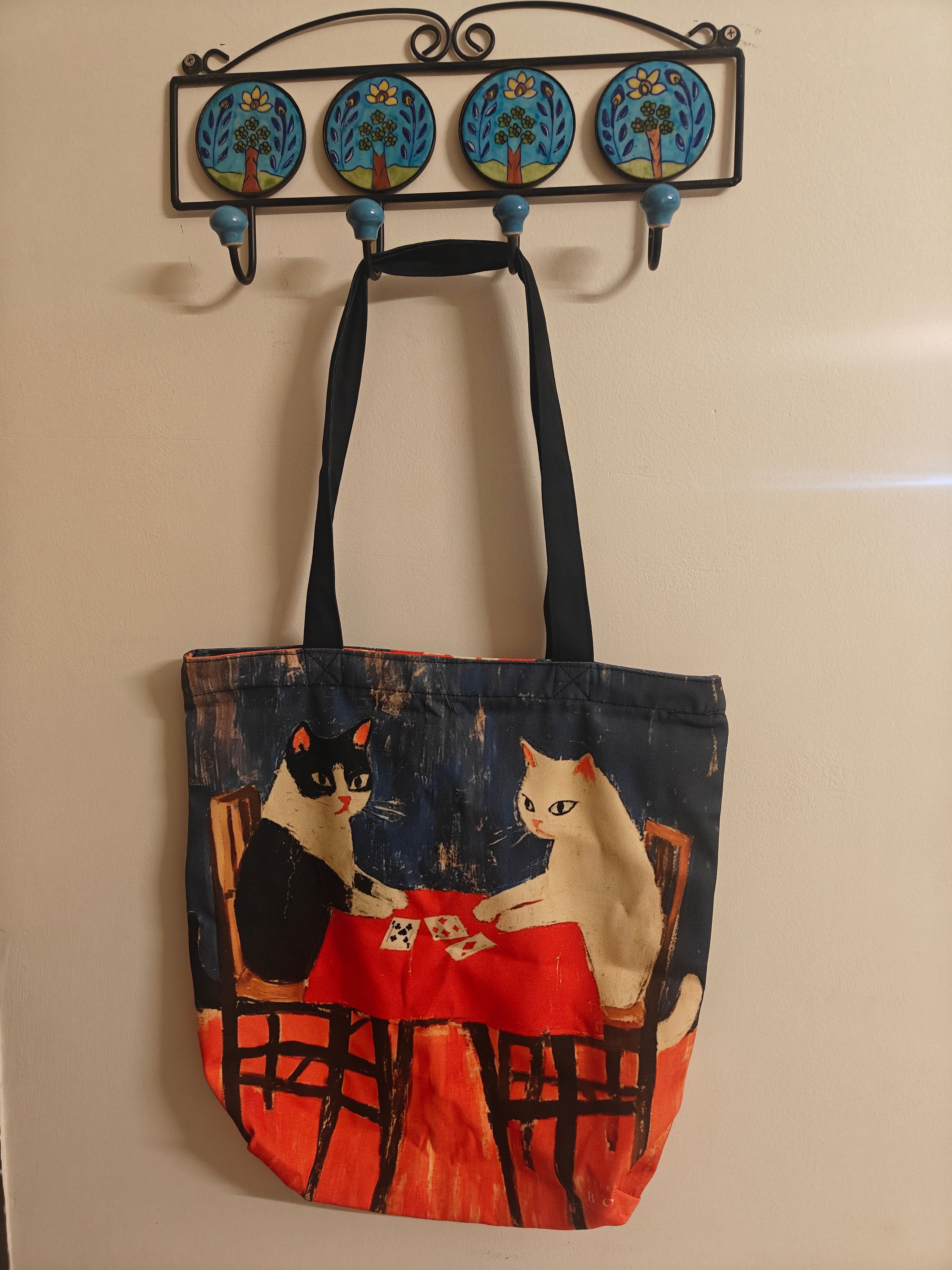 Tote bag with cat design hanging on a decorative hook against a beige wall.
